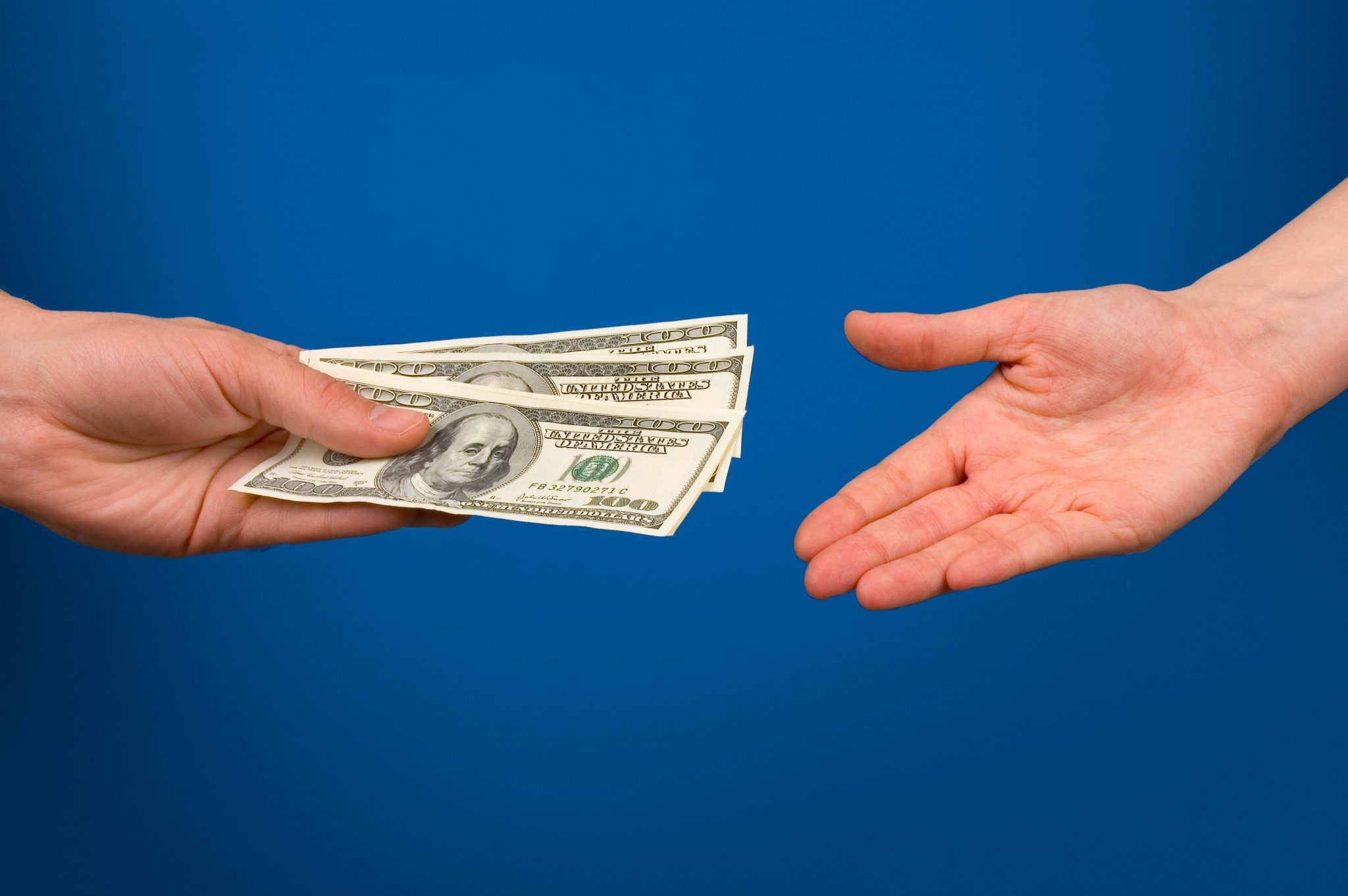 One hand gives money in other hand over blue background
