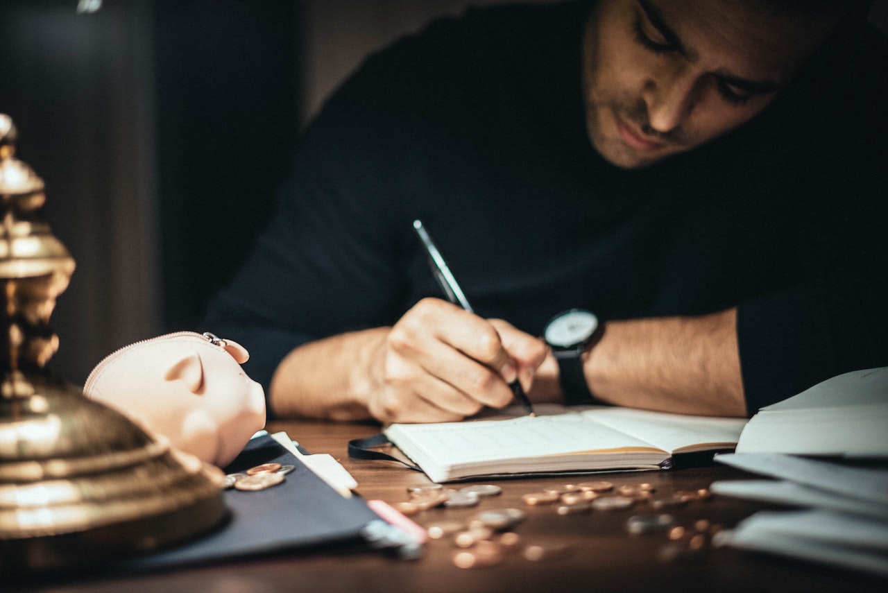Focused man writing in accountant book, checking finances.