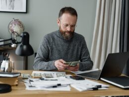 Man in gray sweater counting money into dollar bills.