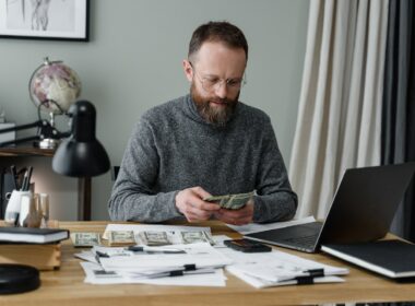 Man in gray sweater counting money into dollar bills.