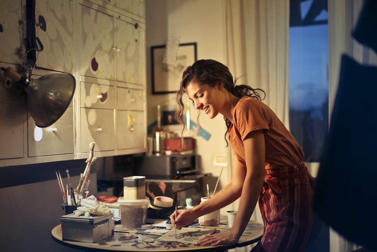 Brunette woman smiling, painting at her kitchen table.