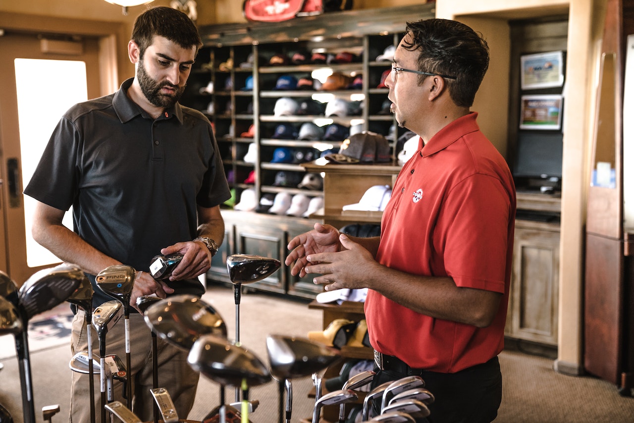 Salesman helping man buy golfclubs at sporting goods store