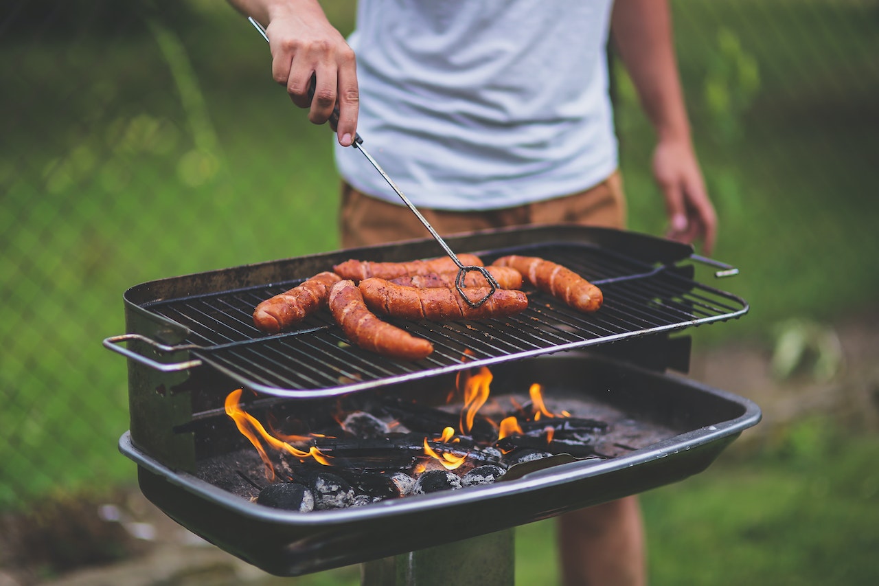 Man grilling hot dogs over charcoal