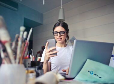 Woman in White T-shirt Holding Smartphone in Front of Laptop