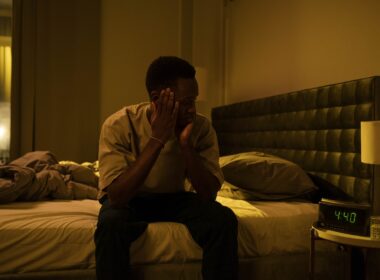Black man sitting on bed looking at clock