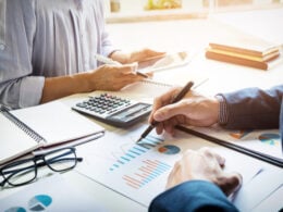 Accountant checking figures with calculator and reports and working with a woman on a project.