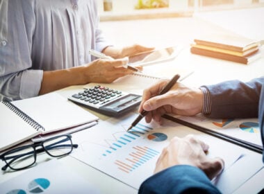 Accountant checking figures with calculator and reports and working with a woman on a project.