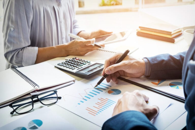 Accountant checking figures with calculator and reports and working with a woman on a project.